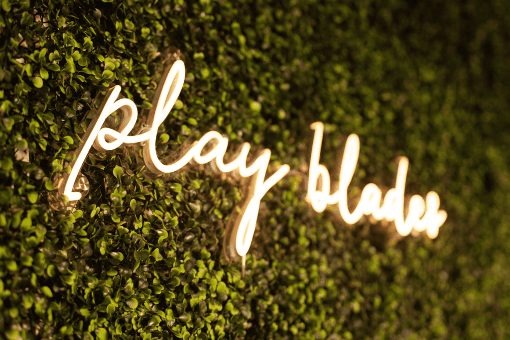 Neon sign 'play blades' on green wall background