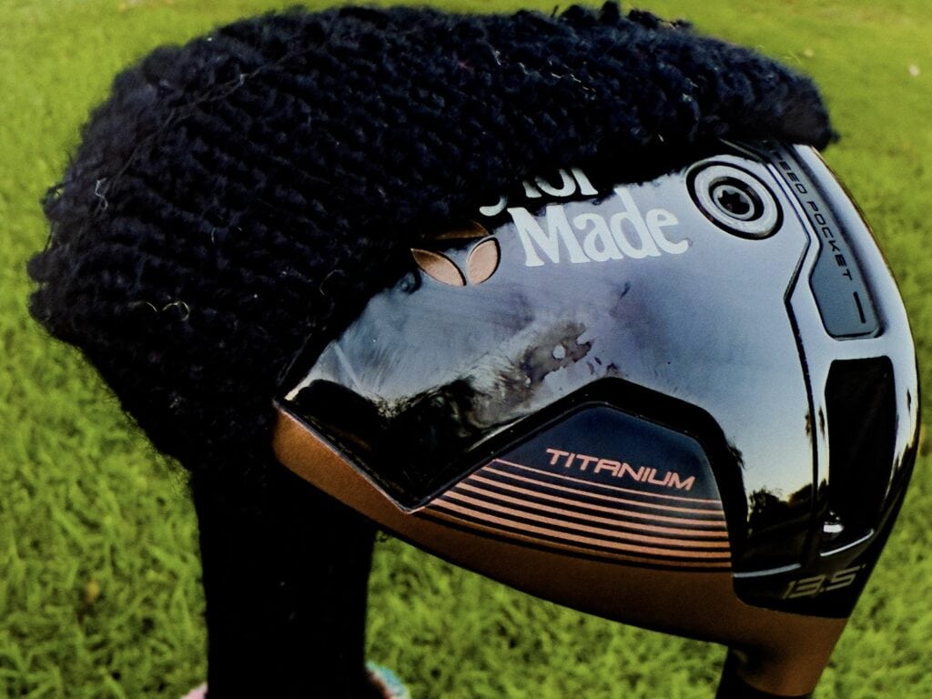 Golf club with black headcover on green grass.